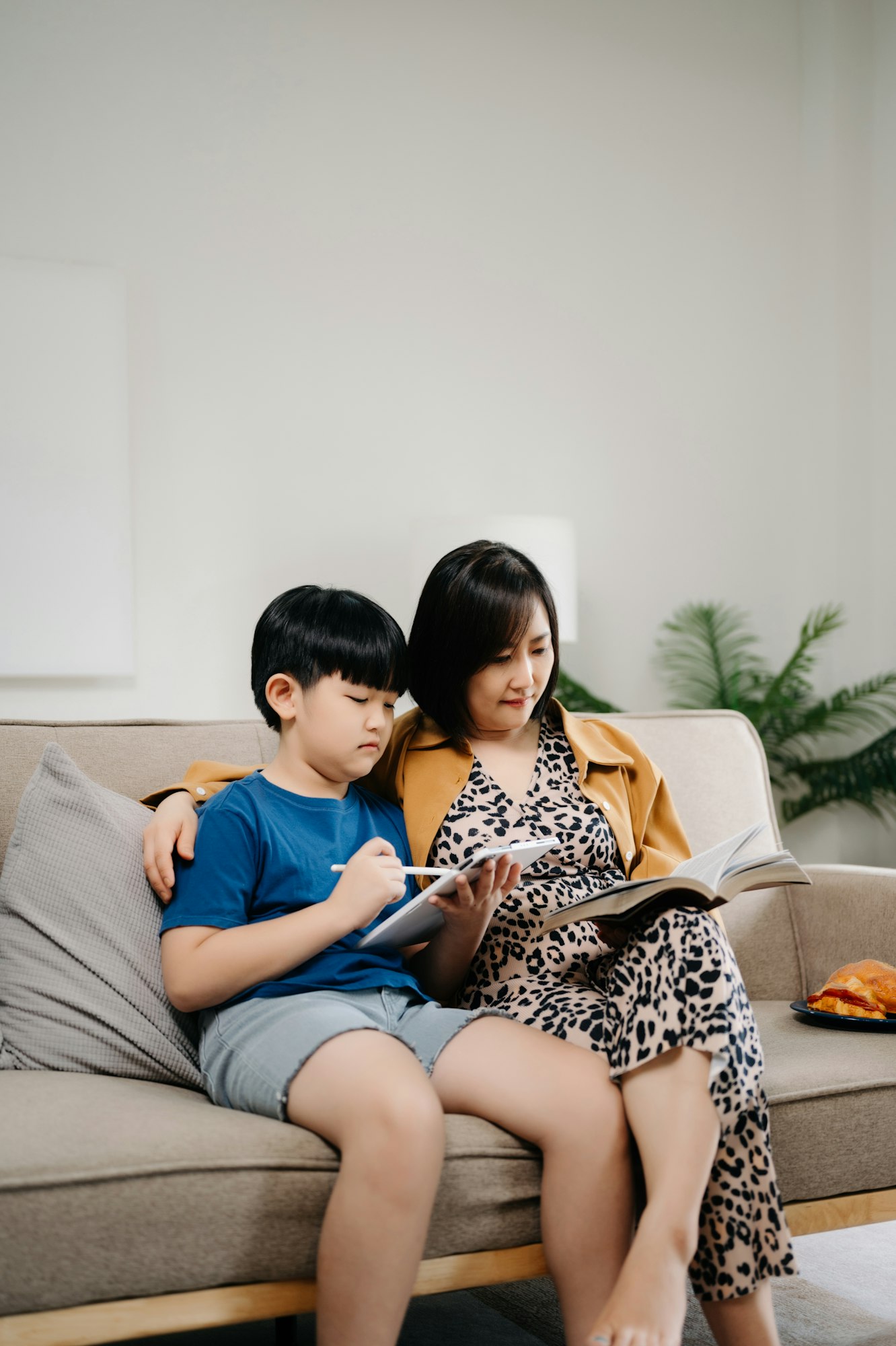 Happy asian mother and son sitting on family couch looking social media on smartphone
