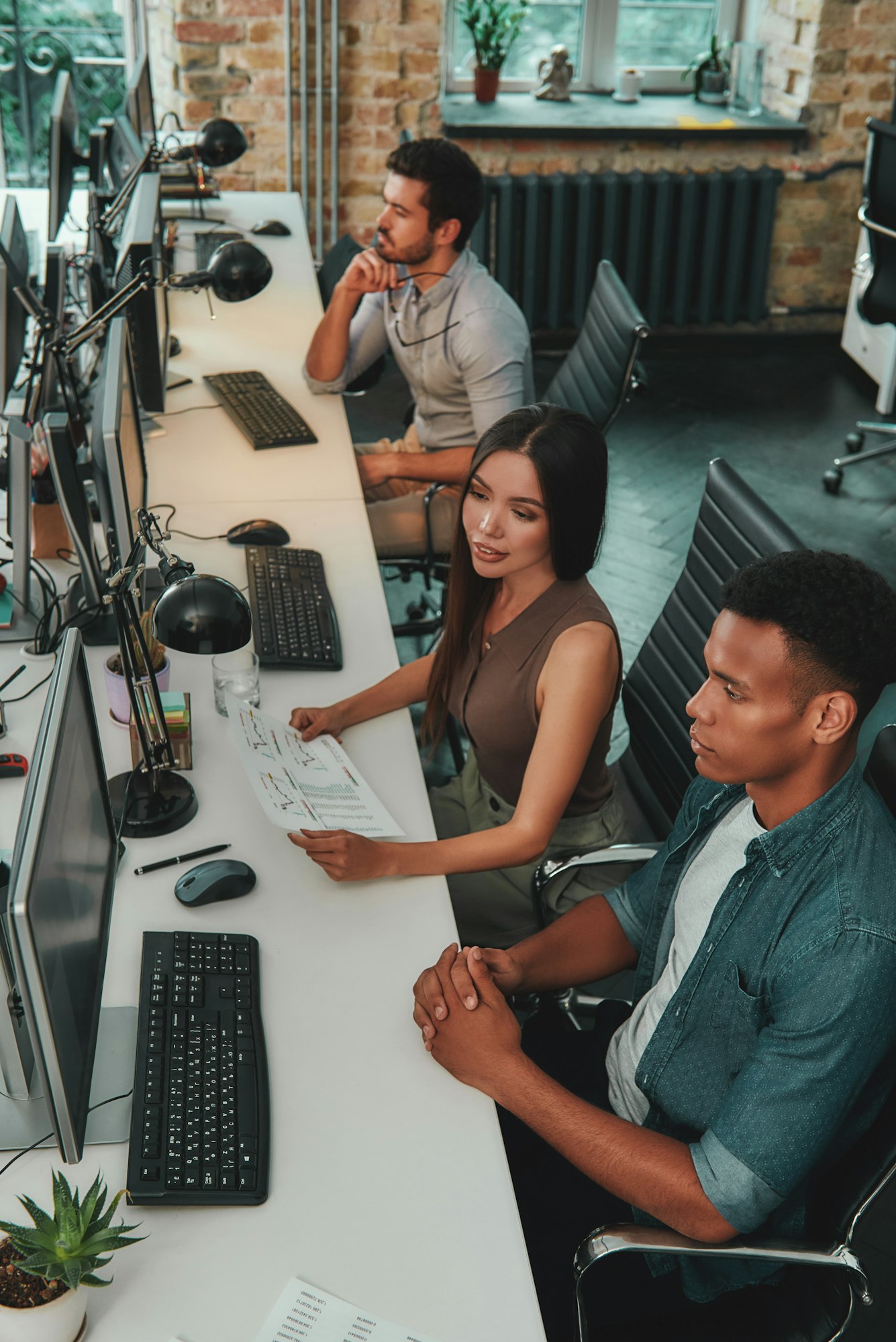 Top view of multiethnic team working on computers and talking with each other while sitting in